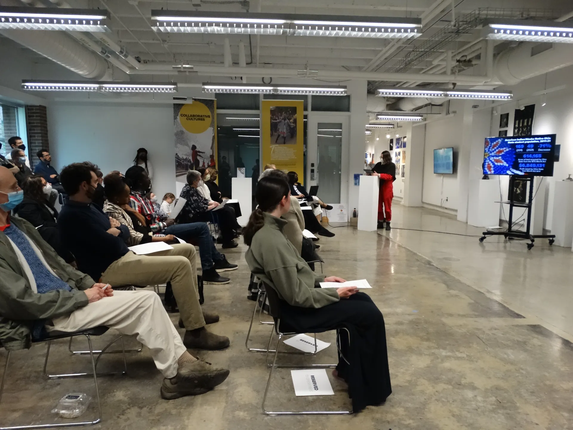 Crowd watches as person presents at white podium