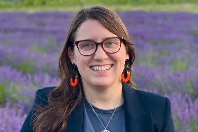 Smiling woman with long hair and glasses standing in field of purple flowers
