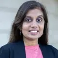 Photograph of woman with long dark hair wearing a dark blazer over a pink blouse